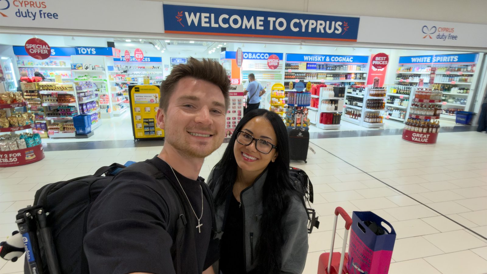 Alex and Megan Colhoun taking a selfie under the Welcome to Cyprus sign at Larnaca Airport