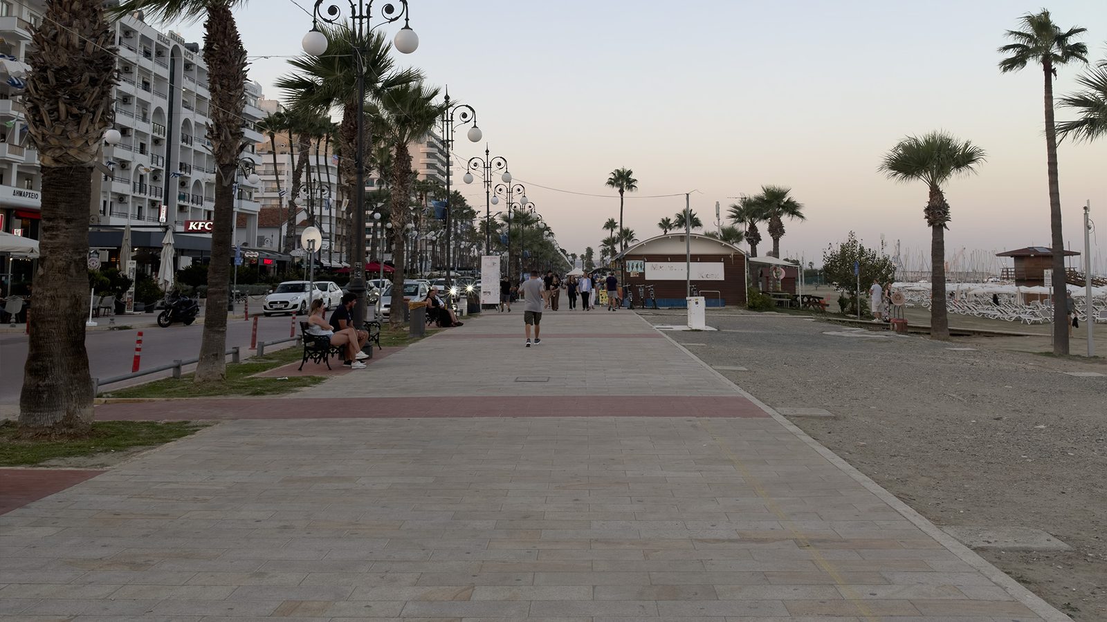 Palm-lined waterfront promenade in Larnaca, Cyprus, at sunset with hotels on one side and the beach on the other