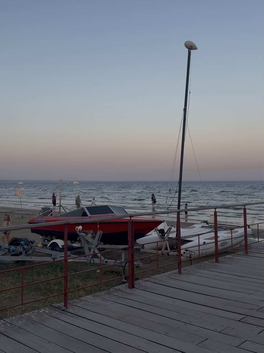 A red speedboat and a small catamaran on the beach in Larnaca at dusk, with people wading in the sea