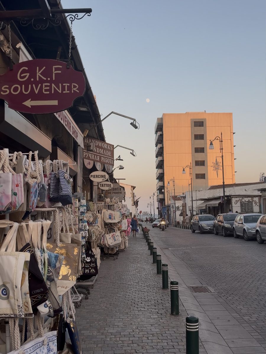 Souvenir shops with tote bags on a cobblestone street in Larnaca at sunset
