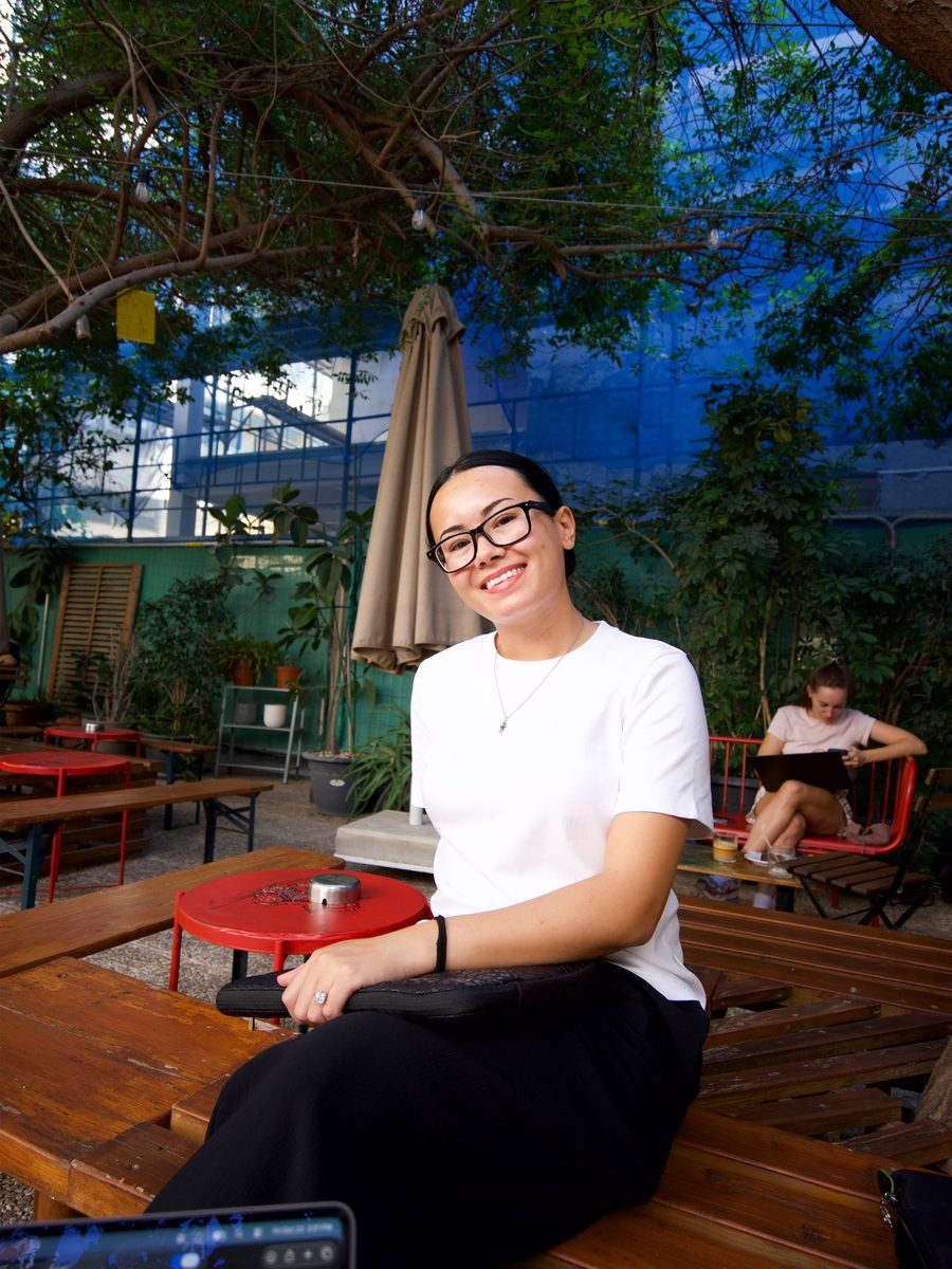 Megan smiling in the tree-shaded courtyard at Paul's Coffee Roasters in Larnaca