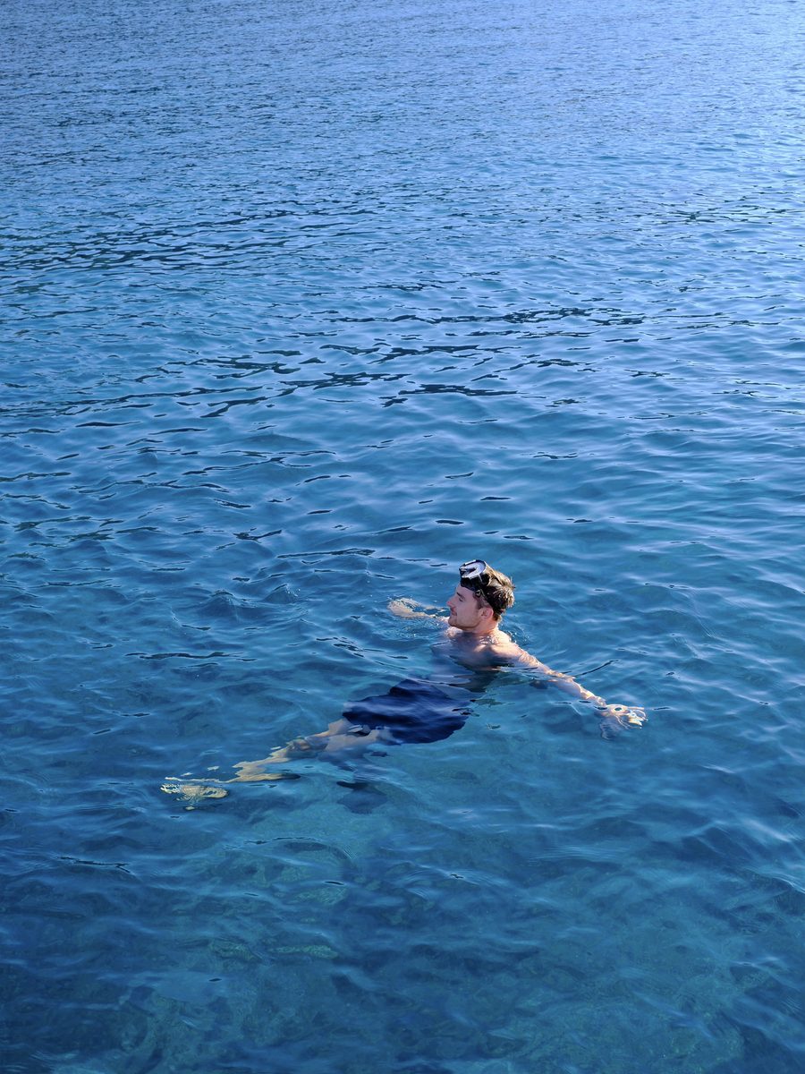 Alex swimming with a snorkel mask in clear blue water during a Santorini catamaran cruise