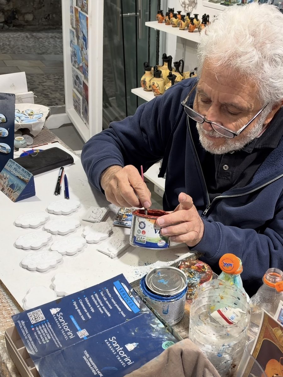 Local artist hand-painting custom souvenir magnets at Black Velvet in Santorini