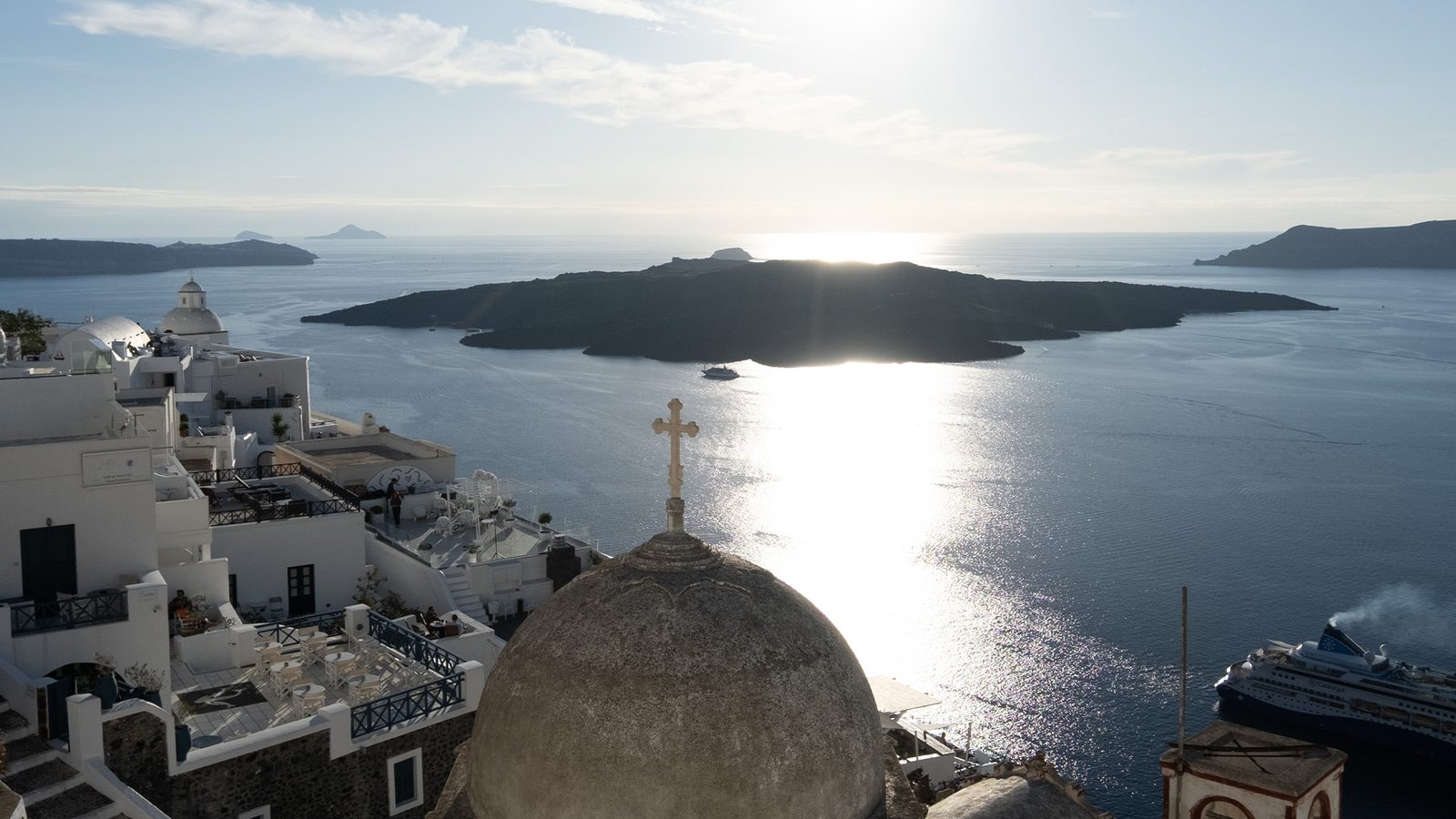 The Santorini caldera and volcano from Fira, with a church dome, white houses and a cruise ship