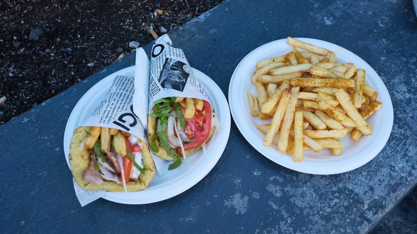 Two gyros pitas with tomato, onion and fries next to a plate of seasoned fries at Good Mood Food in Fira, Santorini