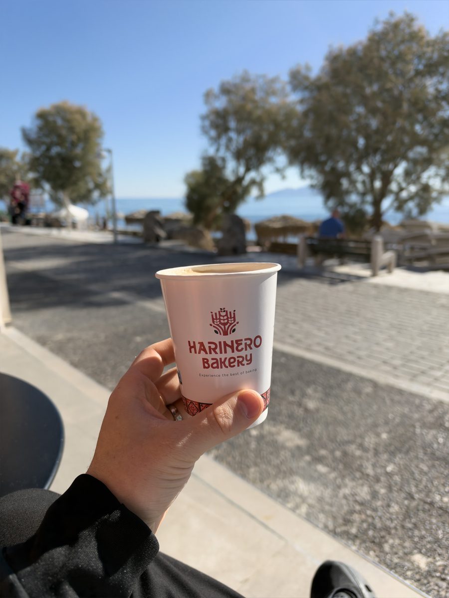Holding a Harinero Bakery latte by the waterfront in Kamari, Santorini