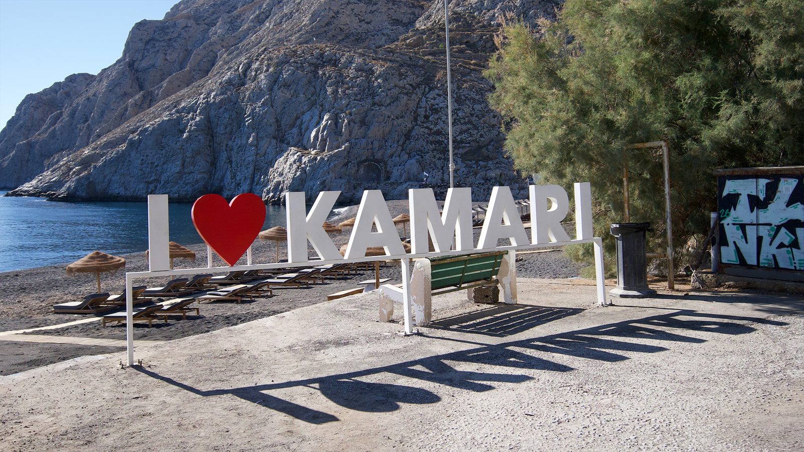 I love Kamari sign on the black sand beach in Kamari, Santorini, with the Mesa Vouno cliff behind