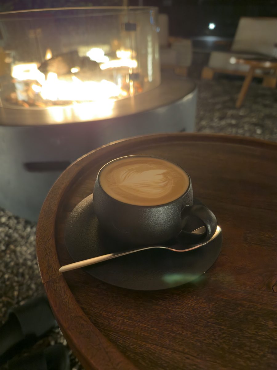 Latte with leaf latte art in a black ceramic cup by the fire pit at Magma Resort, Santorini