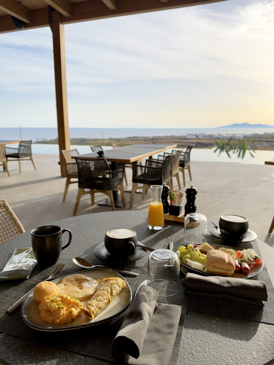 Free breakfast with eggs, pancakes, fruit, coffee and orange juice on the terrace at Magma Resort Santorini, overlooking the sea