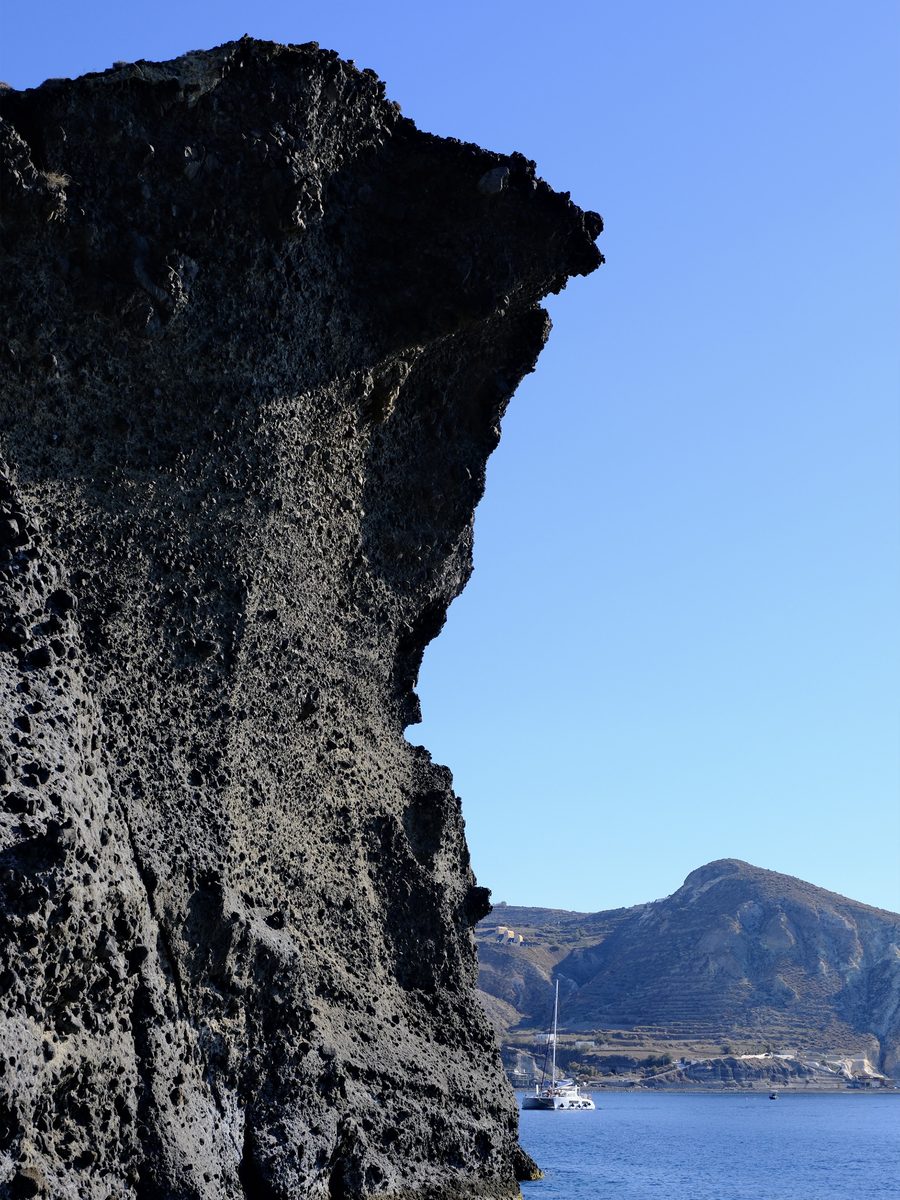 Dark volcanic cliff rising from the sea, seen from a catamaran cruise in Santorini